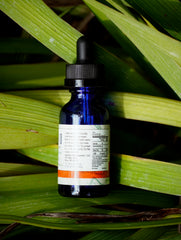 Blue glass dropper bottle with a label on green leaves
